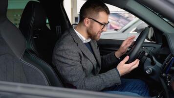 Happy man sits in new electric car in shop dealership and celebrate purchase of new vehicle. Buy car video