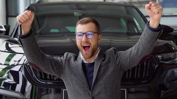 A stylish man with keys rejoices in buying a new car in a car dealership video