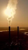 industrie tussen natuur Bij duisternis. dik rook gaan van industrieel pijp in de avond. fabricage in de buurt de rivier- Bij zonsondergang. natuur in Gevaar. verticaal video