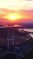 fábrica em colorida céu fundo às pôr do sol. prejudicial fumaça o preenchimento a ar a partir de industrial tubo dentro a tarde. fabricação perto a rio. aéreo visualizar. vertical video