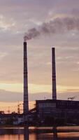 usine dans le campagne. industriel zone près le rivière dans le Matin. nocif fumée Aller dans le air de fabrication parmi soir la nature. verticale video