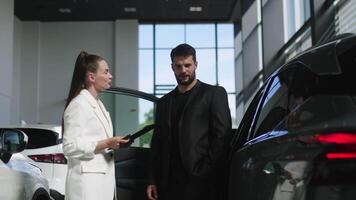 competente coche comerciante utilizando tableta para trabajo con clientela a sala de exposición. hablando con gerente mientras comprando coche a concesión centro. video