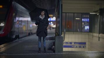 een vrouw onder een elektrisch blauw paraplu Bij een donker trein station video