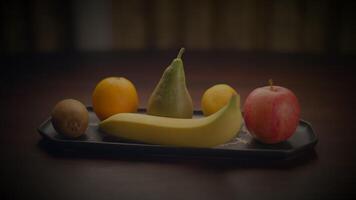un variedad de Fresco frutas desplegado en un bandeja, exhibiendo un sano y vistoso surtido. el escena incluye un banana, pera, naranja, limón, y manzana, arreglado pulcramente en un mesa video