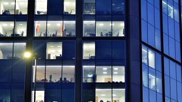 fragmento de el vaso fachada de un moderno corporativo edificio a noche. moderno vaso oficina en ciudad. grande brillante ventanas en moderno oficina edificios a noche, en filas de ventanas ligero brilla foto