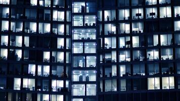 fragmento de el vaso fachada de un moderno corporativo edificio a noche. moderno vaso oficina en ciudad. grande brillante ventanas en moderno oficina edificios a noche, en filas de ventanas ligero brilla foto