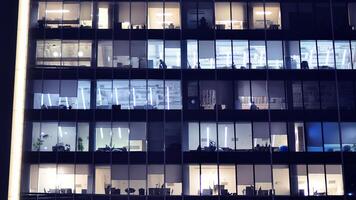 fragmento de el vaso fachada de un moderno corporativo edificio a noche. moderno vaso oficina en ciudad. grande brillante ventanas en moderno oficina edificios a noche, en filas de ventanas ligero brilla foto