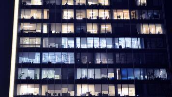 Fragment of the glass facade of a modern corporate building at night. Modern glass office in city. Big glowing windows in modern office buildings at night, in rows of windows light shines. photo