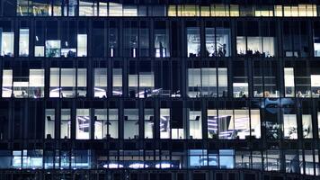 Fragment of the glass facade of a modern corporate building at night. Modern glass office in city. Big glowing windows in modern office buildings at night, in rows of windows light shines. photo