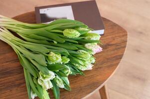 verde y rosado loro tulipanes en de madera mesa con libro. foto