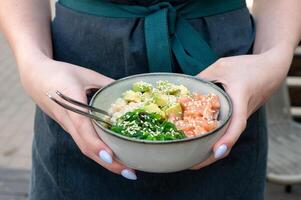A woman holds a traditional Hawaiian poke bowl with fish in her hands. Hawaiian and Japanese cuisine photo
