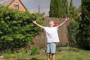 A cute boy is standing on the lawn under drops of water. Close your eyes and stand underwater photo