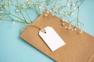 A mock-up of a white tag and a price tag near a craft package with flowers lie on a blue table photo