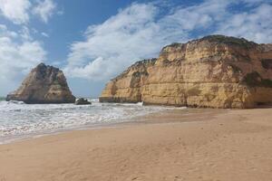 Rocky sea stacks on sandy beach with waves crashing. photo