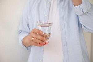 The man's hands are holding a glass of water and pills. photo