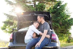 Dad and son are sitting in the trunk of a car at sunset. Hugging Dad photo