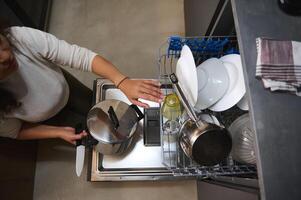 View from above of housewife taking out a stainless steel saucepan, emptying out clean sterilized dishes from a dishwasher. Kitchen appliances. People. Lifestyles. Household. photo