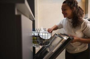 Authentic portrait of a happy smiling woman using a modern dishwasher in the kitchen. Housekeeping. Household chores. People and domestic life routine photo