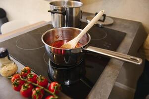 Tomato sauce passata, freshly boiled in stainless steel saucepan on induction stove, prepared from ripe organic eco-friendly tomato cherry - traditional sauce for Italian cuisine. Top view. Copy space photo