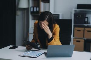 Portrait of tired young business Asian woman work with documents tax laptop computer in office. Sad, unhappy, Worried, Depression, or employee life stress concept photo