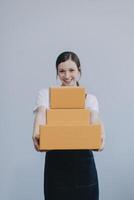 Smiling Asian woman in casual clothes holding a cardboard box mockup while standing against an isolated white background. shipping business concept photo