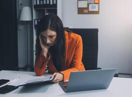 Portrait of tired young business Asian woman work with documents tax laptop computer in office. Sad, unhappy, Worried, Depression, or employee life stress concept photo