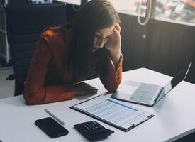 Portrait of tired young business Asian woman work with documents tax laptop computer in office. Sad, unhappy, Worried, Depression, or employee life stress concept photo