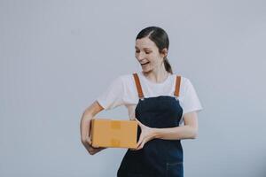 Smiling Asian woman in casual clothes holding a cardboard box mockup while standing against an isolated white background. shipping business concept photo