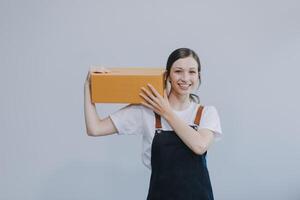 Smiling Asian woman in casual clothes holding a cardboard box mockup while standing against an isolated white background. shipping business concept photo