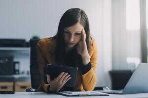 Portrait of tired young business Asian woman work with documents tax laptop computer in office. Sad, unhappy, Worried, Depression, or employee life stress concept photo