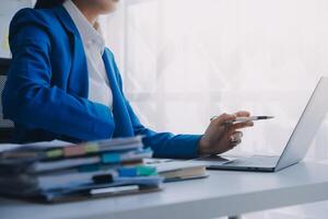 Cheerful business lady working on laptop in office, Asian happy beautiful businesswoman in formal suit work in workplace. Attractive female employee office worker smile. photo