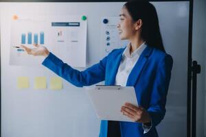 una alegre mujer de negocios que trabaja en una laptop en la oficina, una feliz y hermosa mujer de negocios asiática con traje formal trabaja en el lugar de trabajo. atractiva sonrisa de empleada de oficina. foto