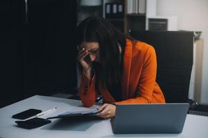 Portrait of tired young business Asian woman work with documents tax laptop computer in office. Sad, unhappy, Worried, Depression, or employee life stress concept photo