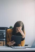 Portrait of tired young business Asian woman work with documents tax laptop computer in office. Sad, unhappy, Worried, Depression, or employee life stress concept photo