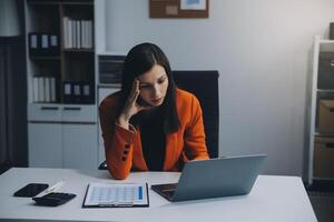 Portrait of tired young business Asian woman work with documents tax laptop computer in office. Sad, unhappy, Worried, Depression, or employee life stress concept photo