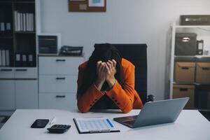 Portrait of tired young business Asian woman work with documents tax laptop computer in office. Sad, unhappy, Worried, Depression, or employee life stress concept photo