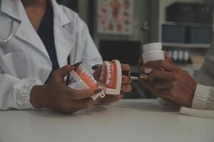 dentista concentrado sentado en la mesa con muestras de mandíbula modelo de diente y trabajando con tableta y computadora portátil en el consultorio dental clínica dental profesional. medico trabajando foto