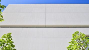 Modern white concrete building walls against blue sky. Eco architecture. Green trees and concrete office building. The harmony of nature and modernity. photo