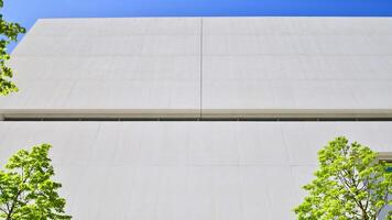 Modern white concrete building walls against blue sky. Eco architecture. Green trees and concrete office building. The harmony of nature and modernity. photo