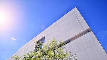 Modern white concrete building walls against blue sky. Eco architecture. Green trees and concrete office building. The harmony of nature and modernity. photo