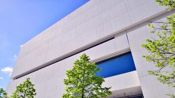 Modern white concrete building walls against blue sky. Eco architecture. Green trees and concrete office building. The harmony of nature and modernity. photo