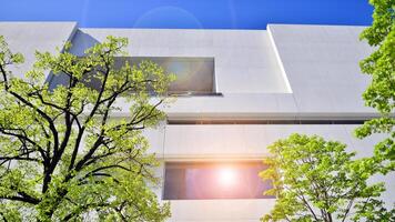 Modern white concrete building walls against blue sky. Eco architecture. Green trees and concrete office building. The harmony of nature and modernity. photo