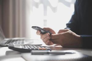 Side view shot of a man's hands using smart phone in interior, rear view of business man hands busy using cell phone at office desk, young male student typing on phone sitting at wooden table, flare photo