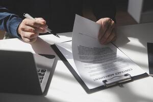 Asian businessman reviewing document reports at office workplace with computer laptop. legal expert, professional lawyer reading and checking financial documents or insurance contract photo