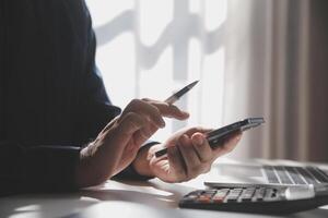 Side view shot of a man's hands using smart phone in interior, rear view of business man hands busy using cell phone at office desk, young male student typing on phone sitting at wooden table, flare photo