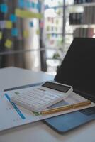 Close up view of simple workspace with laptop, notebooks, coffee cup and tree pot on white table with blurred office room background photo