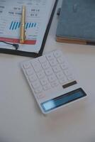 Close up view of simple workspace with laptop, notebooks, coffee cup and tree pot on white table with blurred office room background photo