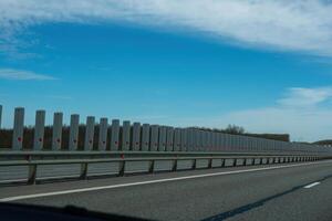 A road with a long line of metal posts with red hearts on them. The road is empty and the sky is clear. photo