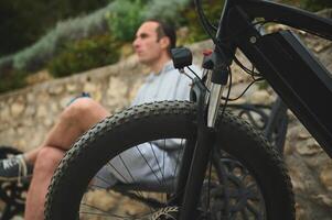 Selective focus on tubeless tire of an electric motor bike, mountain bike over blurred background of male cyclist in the city photo