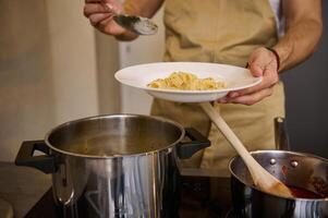 Close-up male chef standing at stove and putting freshly cooked pasta on a white plate photo